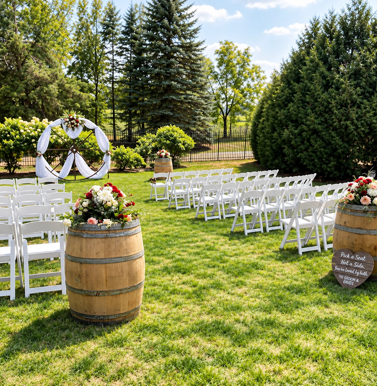 Sunlit outdoor ceremony with white chairs, a draped circular arch, and floral wine barrels beside the aisle