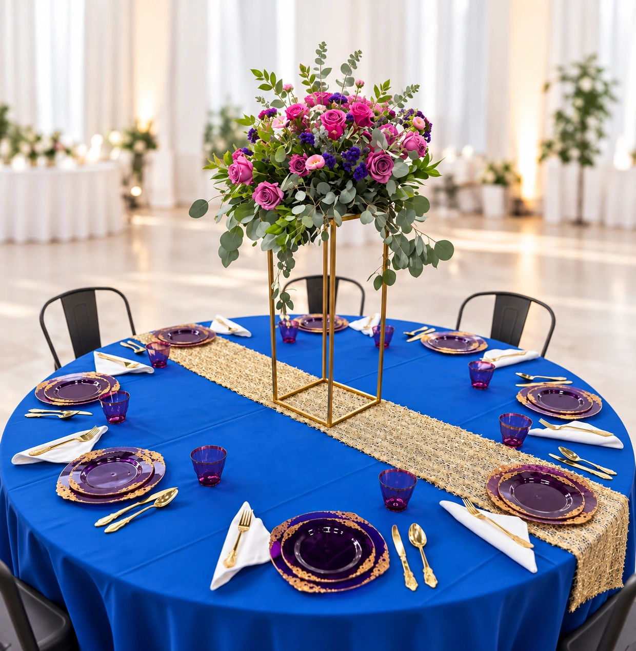 Royal blue reception table with purple and gold place settings, a gold runner, and a complete tall floral centerpiece against a bright white background