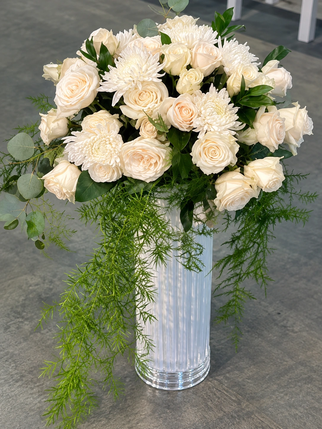 Ivory roses and chrysanthemums with cascading greenery in a tall glass vase